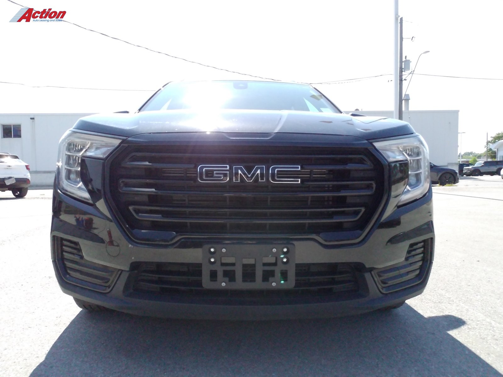 Black GMC truck with a prominent grille captured from the front under bright sunlight.